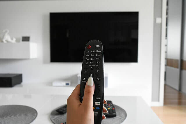 Woman's hand holding a remote control with a TV in the background